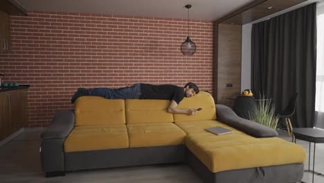 A-man-lays-on-sofa's-rib,-looking-to-a-cell-phone