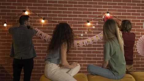Friends-preparing-party-indoors-hanging-garlands-and-hbirthday-letters,-decorating