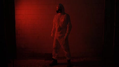 Red-smoke-shot-worker-in-respirator-and-protection-suit-standing-against-brick-wall