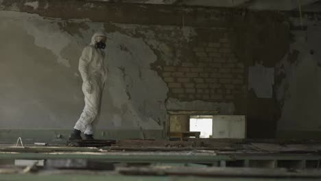 Worker-in-protection-suit-standing-against-destroyed-brick-wall-in-abandoned-building