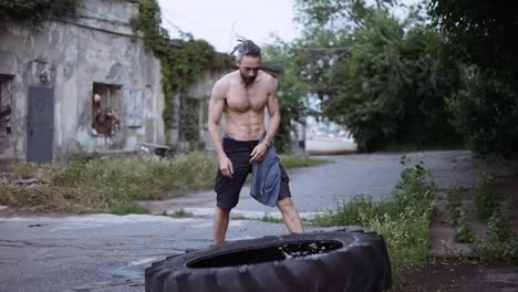 Shirtless-man-pushes-raises-large-wheel-from-tractor-outdoors