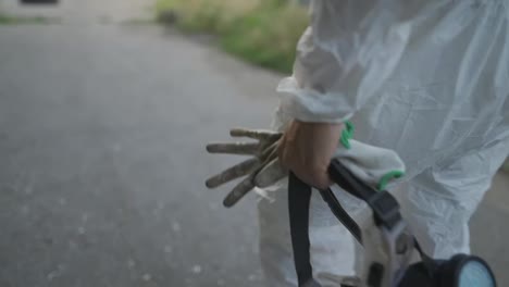 Unrecognizable-worker-in-protective-suit-walks-with-mask-and-gloves-in-hand