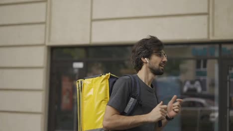 A-bearded-guy-with-a-delivery-backpack-is-fooling-around,-slow-motion