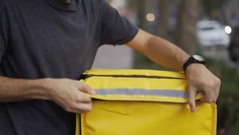 Cheerful-courier-zipping-yellow-backpack,-ready-to-deliver-order