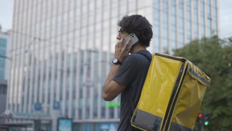 Delivery-man-with-backpack-calling-to-a-client-on-the-city-street