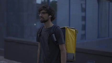 Delivery-man-walking-with-bike-and-yellow-bag-by-modern-city