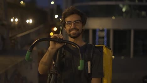 Kurier-Hält-Sein-Fahrrad-Und-Seinen-Rucksack-Draußen-Und-Lächelt