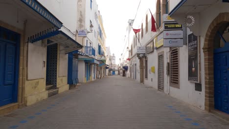Walking-down-an-empty-narrow-street-in-a-city-of-blue-and-white-architecture,-Essaouira,-Morocco