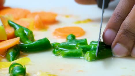 Chef-cutting-green-chili-pepper-closeup-shot-with-some-carrots-in-the-background-and-vegetables-juice-on-the-white-surface