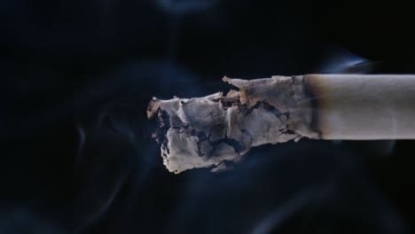 A-Cigarette-smoking-closeup-paper-burning-with-black-background-Ashes-and-Smoke-are-visible-with-soft-Light-on-the-Cigarette