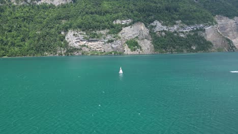 Lonely-yacht-sails-in-turquoise-calm-waters-of-Switzerland-lake,aerial
