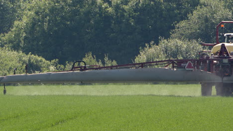 Agricultural-sprayer-pulled-by-tractor-spraying-pesticides-on-crops,-tele-shot