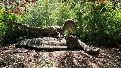 Animated-robot-raptor-dinosaur-standing-over-it's-prey-in-dense-woodland-forest-theme-park-attraction