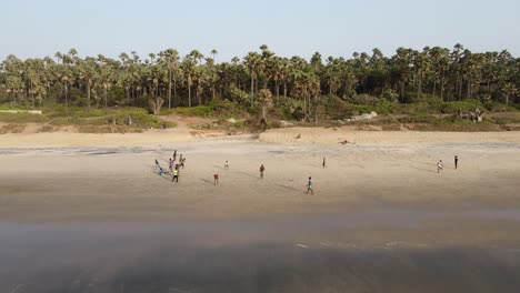 Gambian-children-playing-football-on-the-beach,-filmed-by-a-drone