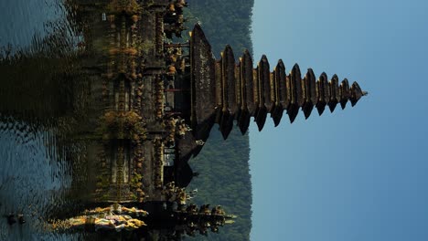 Vertical-slow-motion-panning-shot-of-Pura-Ulun-Danu-temple-with-view-of-volcanic-lake-and-surrounding-nature-with-swimming-ducks