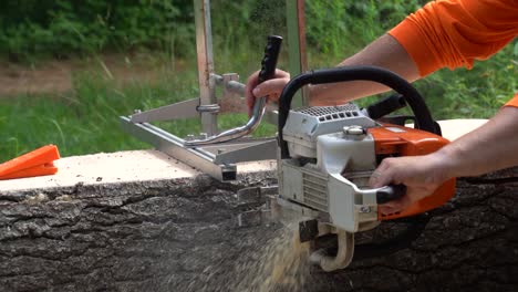 slow-motion-side-shot-of-a-logger-wearing-orange-prepping-a-live-edge-board-from-a-pine-log-using-an-Alaskan-chainsaw-mill
