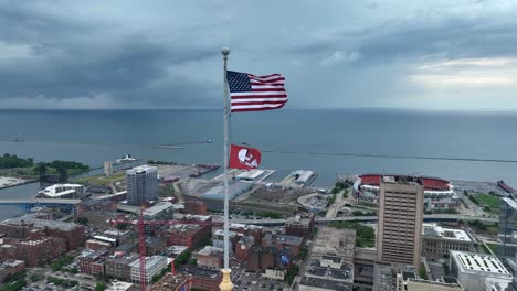 American-National-and-Cleveland-Guardians-Flag-Turned-Upside-Down-Waving-on-Pole-of-Terminal-Tower-With-Lake-Erie-in-Background,-High-Rise-Drone-Shot