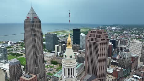Aerial-View-of-Downtown-Cleveland-OH-USA-Towers-and-Waving-American-Flag-on-Terminal-Tower-Residences,-High-Rise-Orbiting-Drone-Shot