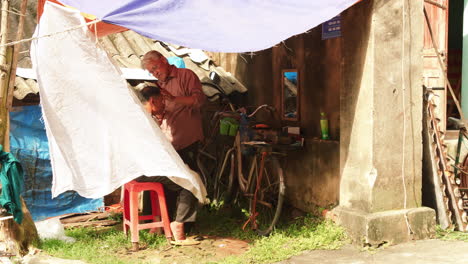 Mobile-hairdresser-cuts-mans-hair-with-a-razor-in-a-street-market,-Vietnam