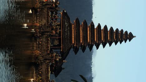 Vertical-unveiling-shot-of-Pura-Segara-Ulun-Danu-a-spiritual-temple-in-the-water-on-Bali-with-reflecting-water-and-view-of-ducks,-nature-and-the-golden-hour