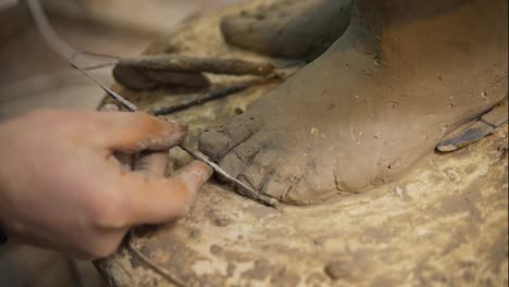 Close-up-of-clay-Buddha's-statue-feet,-artist-works-with-detail-using-spatula