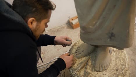 High-angle-view-of-clay-Buddha's-statue-feet,-artist-works-with-detail-using-tools