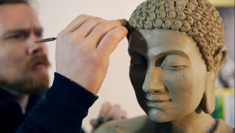 Bearded-man-working-on-Buddha-statue-hair-using-a-special-tool-at-workshop