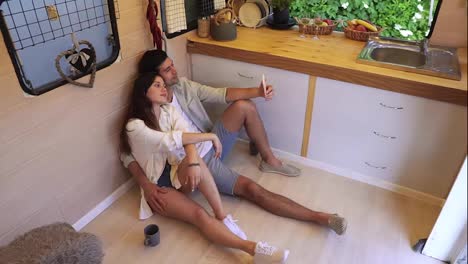 Beautiful-couple-sitting-on-the-floor-in-the-stylish-kitchen-in-van-and-doing-selfie-using-smartphone,-posing-.-Enjoying-togetherness,-shared-holidays,-traveling-by-wheels-house.-Modern-interior.-High-angle-footage