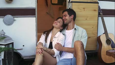 Lovely-portrait-of-a-young-couple.-They-are-sitting-on-the-stairs-of-their-modern-trailer,-embracing-and-smiling.-Dreaming-and-thoughtful-mood