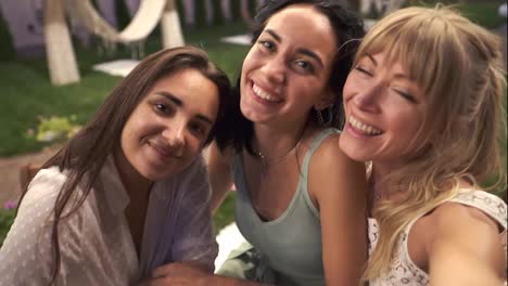 Three-joyful-women-met-in-veranda-cafe-outdoors-taking-selfie-photo-or-video-on-smartphone,-having-fun,-drink
