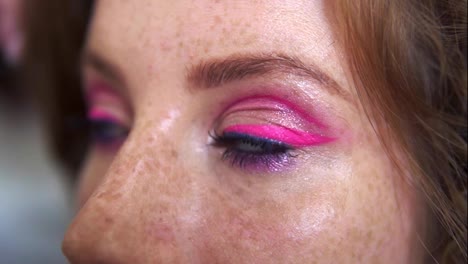 Unrecognizable-makeup-artist-work-in-beauty-studio.-Woman-applying-tone-using-brush.-Artist-make-a-makeup-for-redhead-model-with-freckles.-Close-up-of-eyes-of-a-pretty-girl-with-pink-glitering-make-up