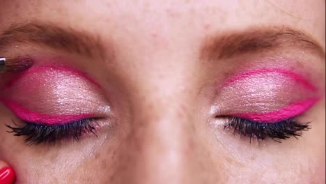 Close-up-of-the-eyes-of-a-young-woman-during-professional-makeup.-The-makeup-artist-applies-pink-shadows-on-the-girl-s-eye-with-a-brush.-fashion-and-beauty