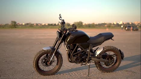A-black-motorcycle-parking-on-the-ground-outdoors,-green-strip-of-trees-on-background