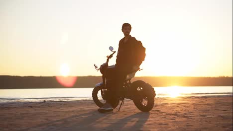 Footage-of-a-male-biker-leaning-on-his-bike-alone-in-front-the-water-in-sunlight