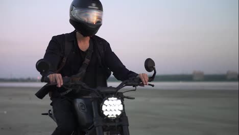 Concentrated-biker-rides-on-black-sport-bike-in-helmet-with-switched-front-headlight.-Evening-dusk