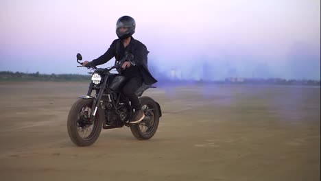 Young-biker-in-black-riding-while-the-engine-blowing-out-blue-exhaust-smoke,-holi