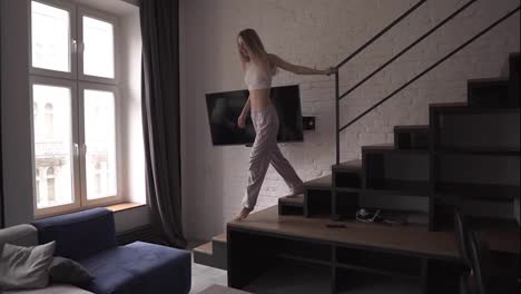 Young-caucasian-woman-in-pajamas-jumping-on-a-couch-running-from-the-stairs-at-home