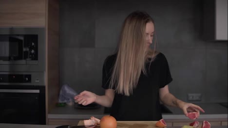 Positive-woman-cleaning-grapefruit-peel-on-chopping-board-at-kitchen-and-dancing