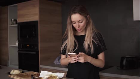 Shot-of-young-woman-using-her-mobile-phone-in-the-kitchen-at-home-in-the-morning