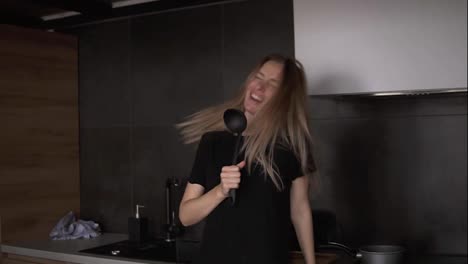 A-cheerful-woman-with-a-ladle-in-a-modern-kitchen-pretends-to-sing