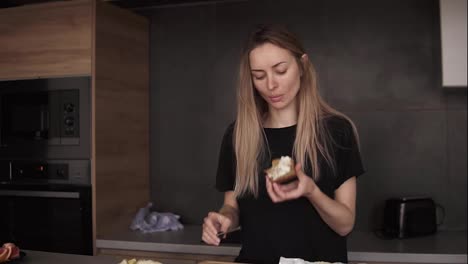 Blonde-Frau-Isst-Brot-Mit-Butter-Zum-Frühstück-Und-Schaut-In-Der-Küche-Auf-Ihr-Smartphone