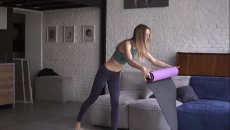 Young-sporty-girl-unfolding-fitness-mat-on-floor-at-home