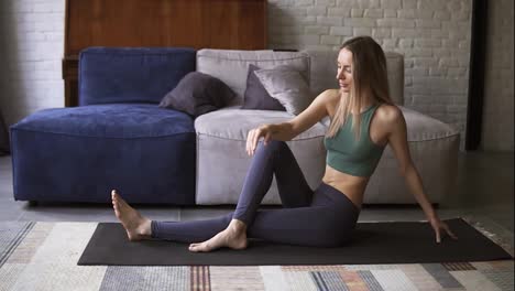Sporty-fit-young-woman-is-doing-stretching-exercise-sitting-on-mat-in-living-room