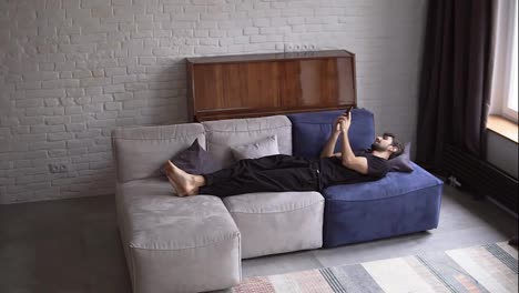 Man-lying-on-couch-using-smartphone,-scrolling-various-gestures-like-swiping-and-scrolling