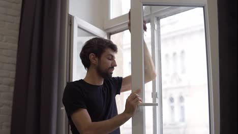 Mann-Putzt-Fenster,-Reinigt-Oberfläche-Und-Benutzt-Einen-Lappen-Und-Steht-In-Einer-Modernen-Wohnung