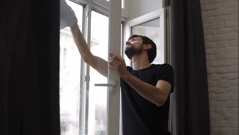 Mann-Putzt-Fenster,-Reinigt-Oberfläche,-Benutzt-Einen-Lappen-Und-Steht-In-Einer-Modernen-Wohnung