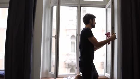 Bearded-man-is-cleaning-window,-cleans-surface,-uses-a-rag,-standing-in-modern-apartment