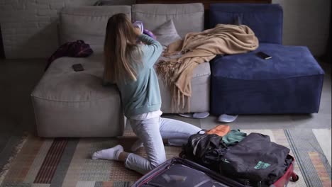A-woman-in-a-living-room-puts-things-in-a-suitcase,-slowmo