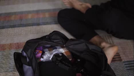Unrecognizable-man-packing-black-bag-with-clothes-for-travel-in-living-room,-close-up