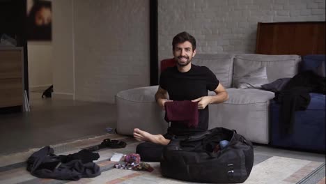 Portrait-of-a-smiling-man-packing-his-back-for-travel-in-living-room